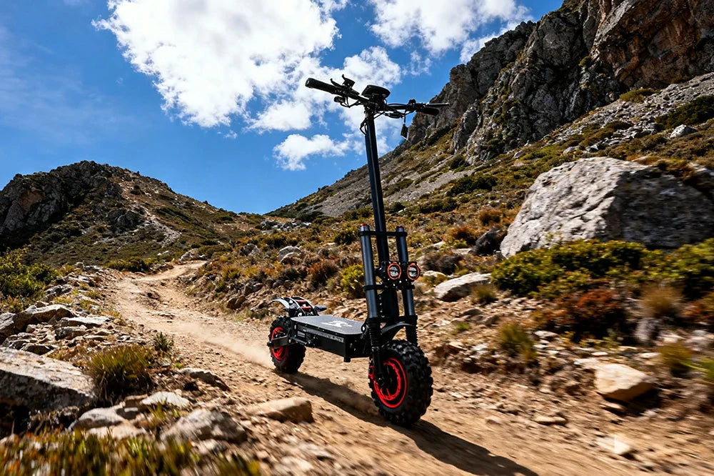 Black-red J30 Max heavy-duty all-terrain e-scooter with thick knobby off-road tires and dual front headlights, traveling on rugged stony alpine trail amid jagged rocky cliffs and wild shrubs